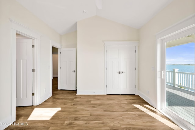 unfurnished bedroom with light wood-type flooring, a water view, lofted ceiling, and access to exterior