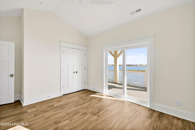 unfurnished bedroom with lofted ceiling, a water view, access to exterior, ceiling fan, and light wood-type flooring