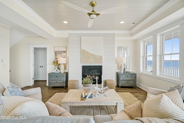 living room featuring dark hardwood / wood-style flooring, wood ceiling, a large fireplace, a water view, and ceiling fan