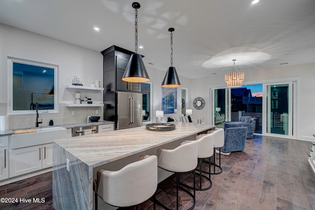 kitchen with sink, a kitchen island, dark wood-type flooring, pendant lighting, and high end fridge