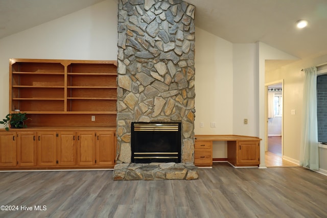 unfurnished living room featuring hardwood / wood-style flooring, vaulted ceiling, and a stone fireplace