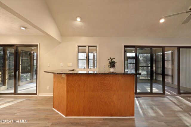 kitchen with dark stone counters, ceiling fan, wood-type flooring, and vaulted ceiling