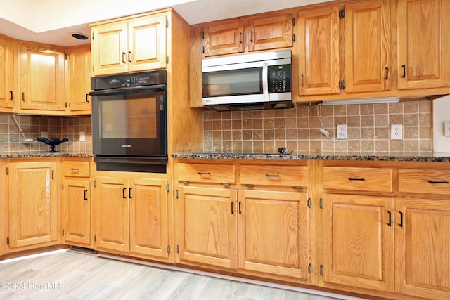 kitchen featuring backsplash, light hardwood / wood-style floors, dark stone countertops, and black appliances