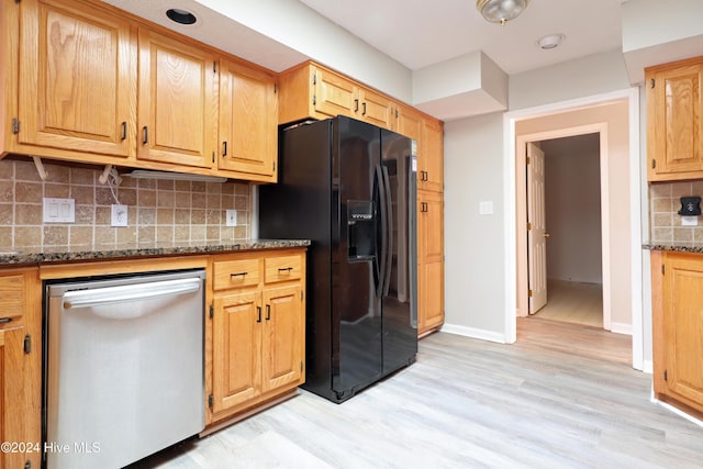 kitchen with dishwasher, black fridge, light hardwood / wood-style flooring, stone countertops, and decorative backsplash