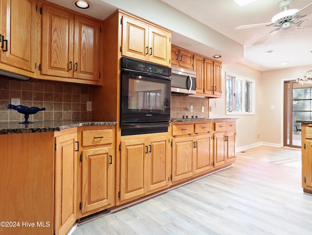 kitchen with black appliances, ceiling fan with notable chandelier, dark stone countertops, tasteful backsplash, and light hardwood / wood-style floors