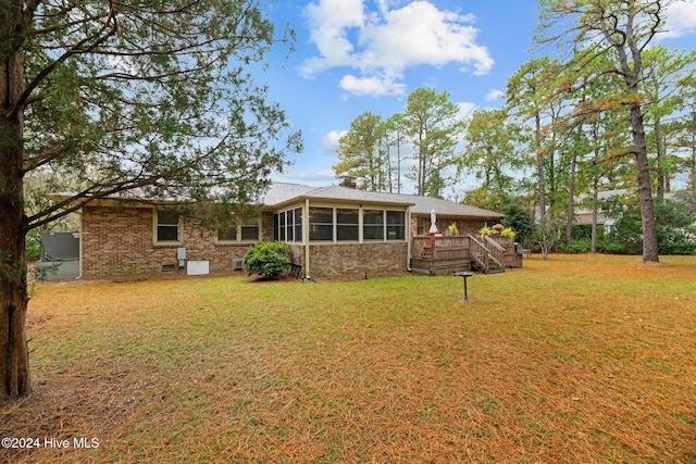 rear view of property featuring a deck, a sunroom, and a yard