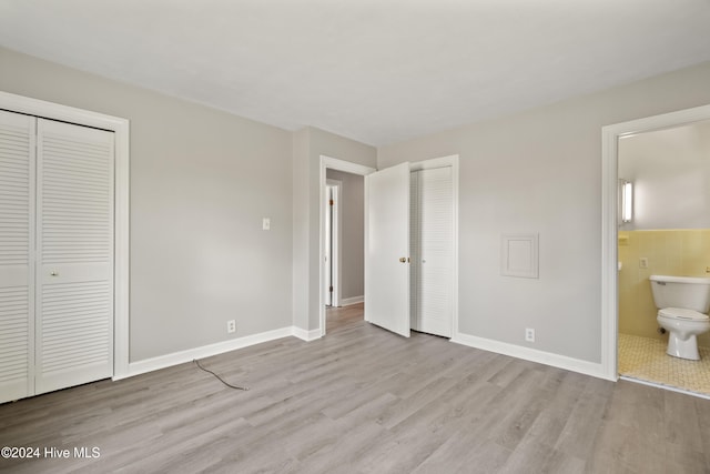 unfurnished bedroom with tile walls, ensuite bath, light hardwood / wood-style floors, and two closets