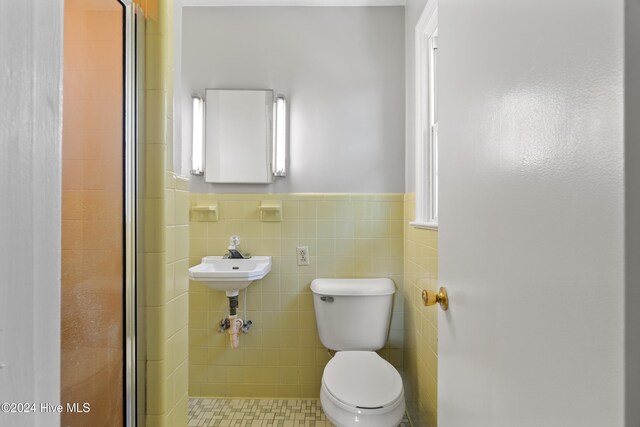 bathroom featuring toilet, a shower with shower door, and tile walls