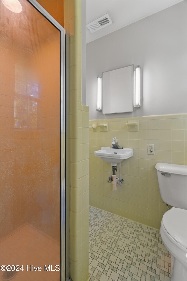 bathroom featuring a shower with door, tile walls, and toilet