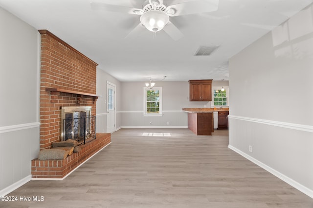 unfurnished living room featuring a fireplace, ceiling fan with notable chandelier, and light hardwood / wood-style flooring