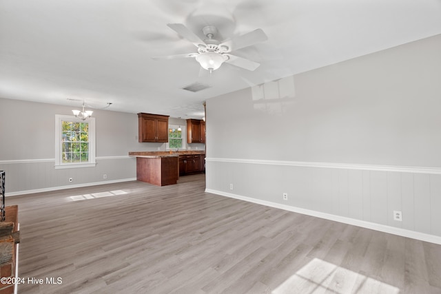 unfurnished living room featuring ceiling fan with notable chandelier and light wood-type flooring