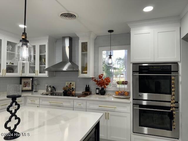 kitchen featuring stainless steel double oven, white cabinetry, hanging light fixtures, and wall chimney range hood