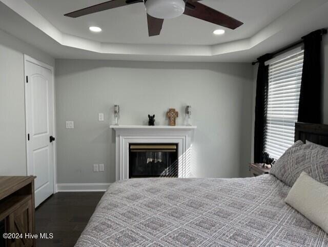 bedroom with dark hardwood / wood-style flooring, a raised ceiling, and ceiling fan