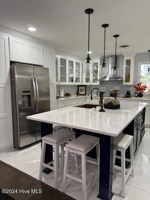 kitchen with stainless steel fridge, a center island with sink, white cabinets, and sink