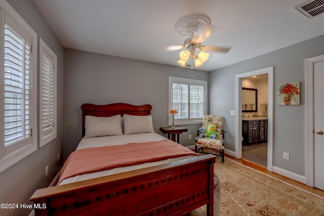 bedroom with light wood finished floors, baseboards, visible vents, a ceiling fan, and ensuite bathroom