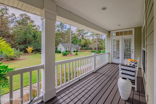 wooden terrace featuring a porch, an outbuilding, and a lawn