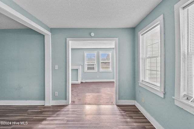 spare room with cooling unit, wood finished floors, baseboards, and a textured ceiling