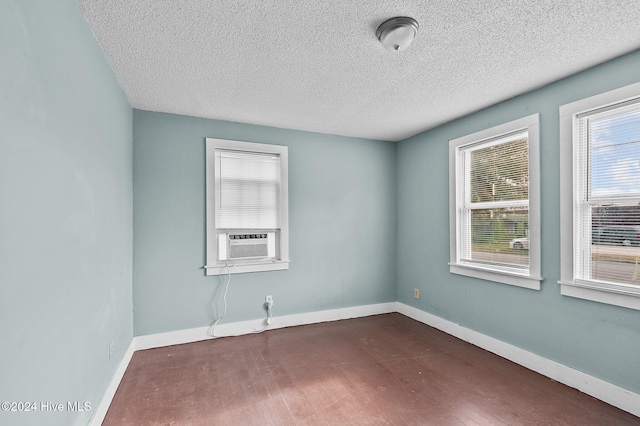 empty room featuring cooling unit, dark wood-style floors, baseboards, and a textured ceiling