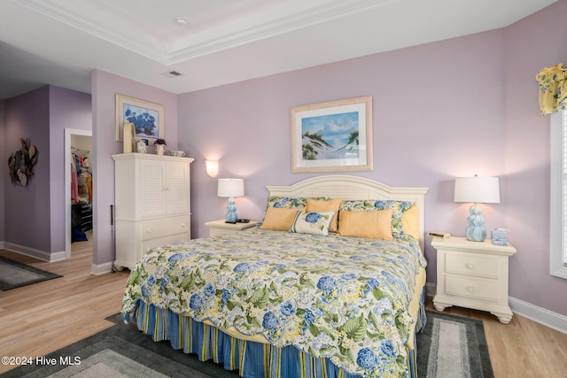 bedroom featuring light hardwood / wood-style flooring, crown molding, a walk in closet, and a closet