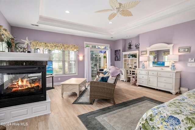 bedroom with ceiling fan, light hardwood / wood-style floors, and a raised ceiling