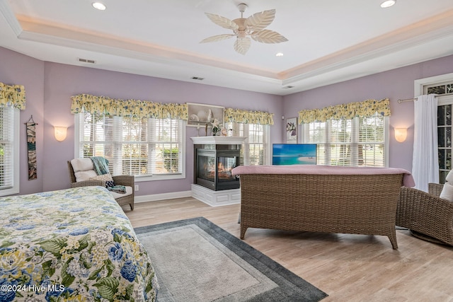 bedroom with light hardwood / wood-style flooring, ceiling fan, and a raised ceiling