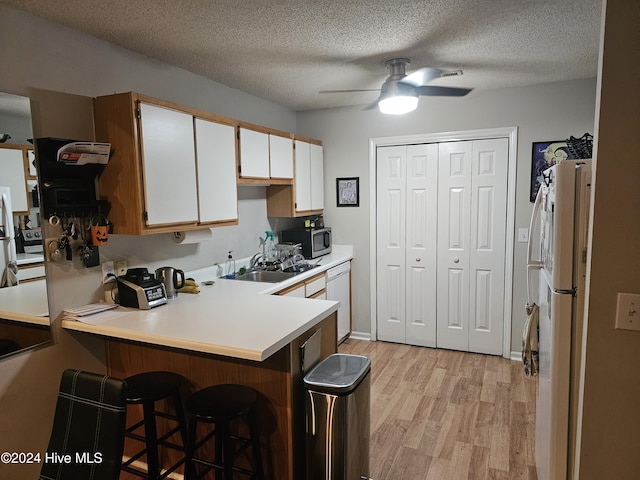 kitchen featuring white appliances, light wood finished floors, a breakfast bar, a peninsula, and light countertops