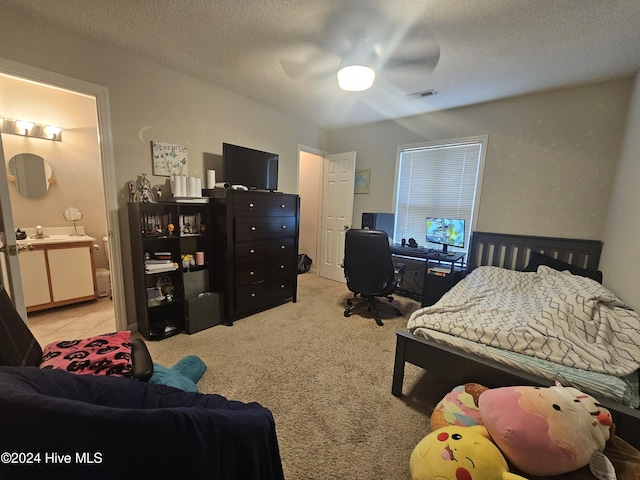 carpeted bedroom featuring visible vents, a ceiling fan, ensuite bathroom, a textured ceiling, and a sink