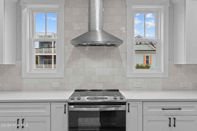 kitchen featuring a healthy amount of sunlight, white cabinets, wall chimney exhaust hood, and stainless steel electric stove