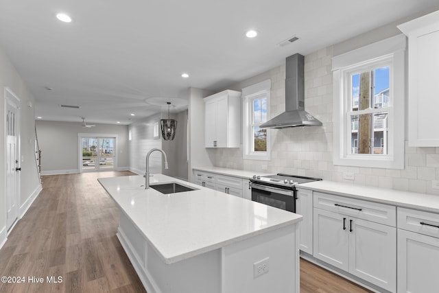 kitchen featuring a center island with sink, stainless steel electric range oven, a sink, wall chimney range hood, and backsplash