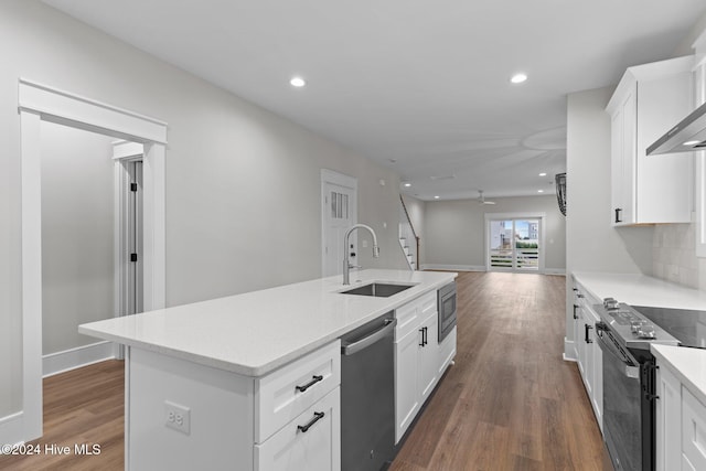 kitchen featuring dark wood finished floors, a sink, a kitchen island with sink, stainless steel appliances, and backsplash