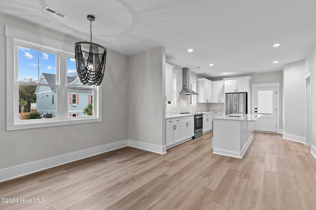 kitchen featuring light wood-style flooring, stainless steel appliances, visible vents, light countertops, and wall chimney range hood