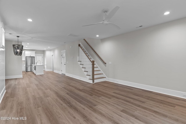 unfurnished living room featuring recessed lighting, light wood-style flooring, baseboards, and stairs