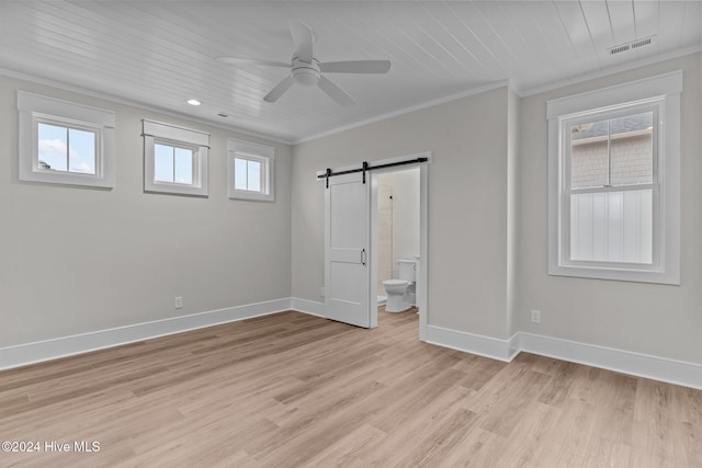 spare room featuring baseboards, a barn door, visible vents, and crown molding