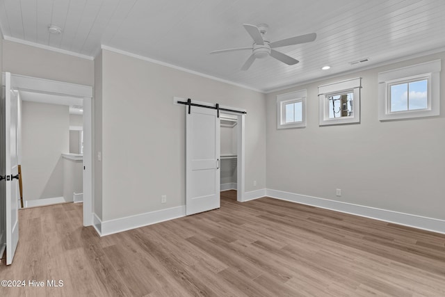 unfurnished bedroom featuring light wood finished floors, a barn door, baseboards, and crown molding