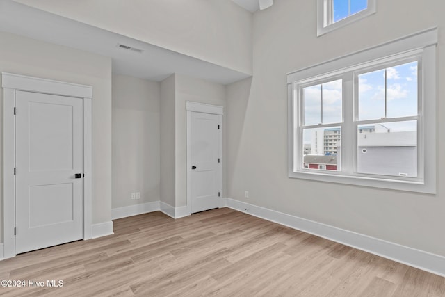 empty room with light wood-type flooring, visible vents, and baseboards