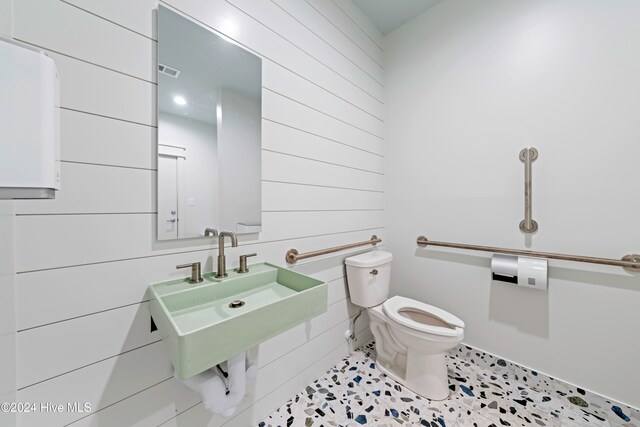 half bathroom featuring tile patterned flooring, a sink, wood walls, and toilet