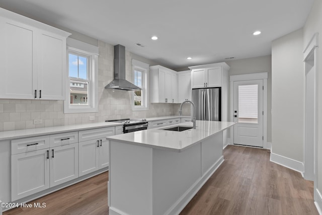 kitchen with stainless steel appliances, wood finished floors, a sink, light countertops, and wall chimney range hood