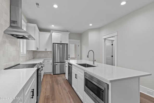 kitchen with stainless steel appliances, backsplash, a sink, wall chimney range hood, and wood finished floors