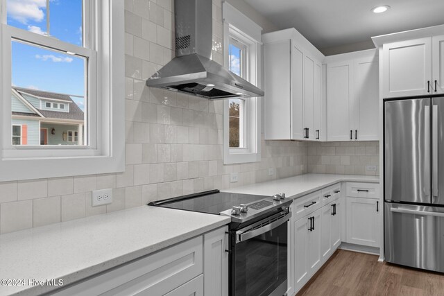 kitchen with tasteful backsplash, wall chimney exhaust hood, appliances with stainless steel finishes, wood finished floors, and white cabinetry