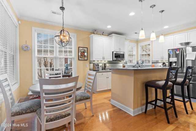 4151 Windham Ln, Southport, NC 28461 - kitchen with stainless steel appliances, a chandelier, ornamental molding, a kitchen breakfast bar, and white cabinetry