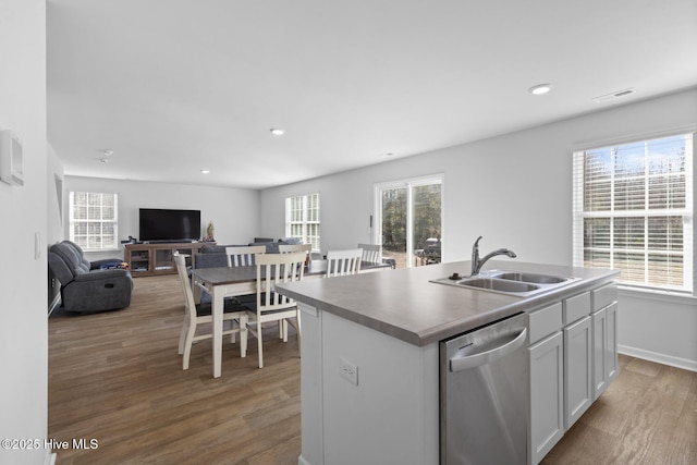 kitchen with light wood-type flooring, stainless steel dishwasher, sink, a center island with sink, and white cabinetry