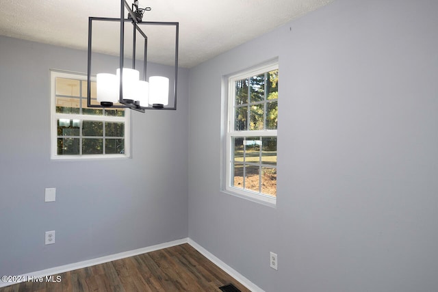 unfurnished dining area with dark hardwood / wood-style flooring, a chandelier, a textured ceiling, and a healthy amount of sunlight