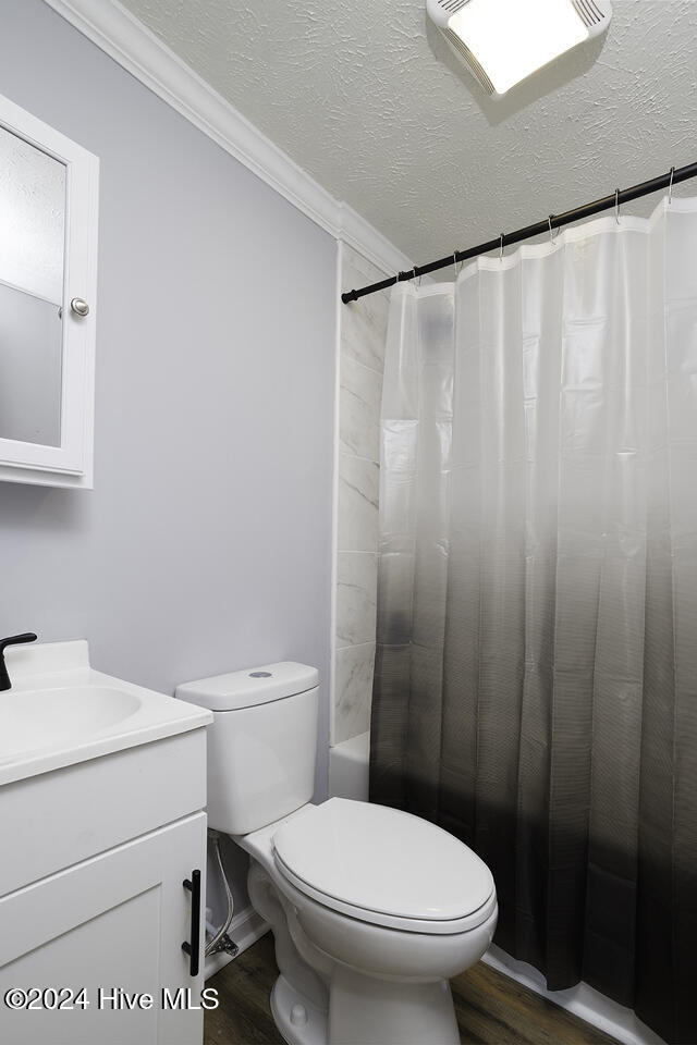 full bathroom with vanity, hardwood / wood-style flooring, a textured ceiling, and crown molding