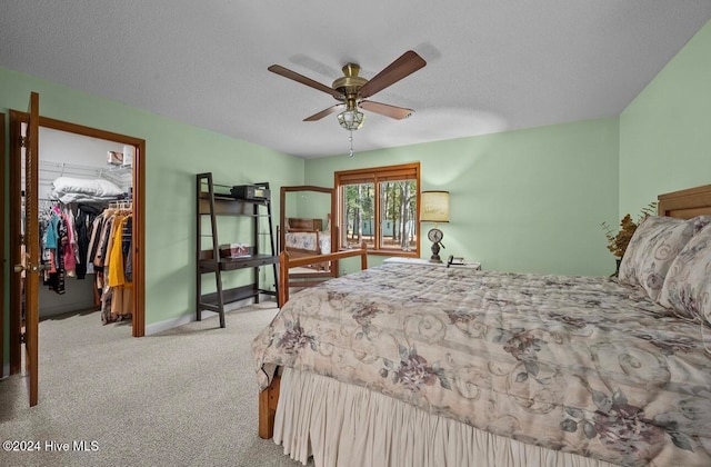 bedroom featuring a walk in closet, ceiling fan, a textured ceiling, light colored carpet, and a closet