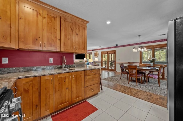 kitchen with sink, pendant lighting, light tile patterned floors, an inviting chandelier, and stainless steel refrigerator