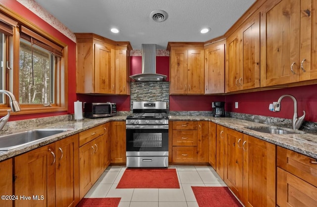 kitchen featuring appliances with stainless steel finishes, sink, light stone counters, and wall chimney range hood