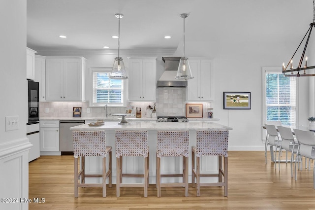 kitchen with light wood-type flooring, stainless steel dishwasher, wall chimney exhaust hood, white cabinets, and a center island