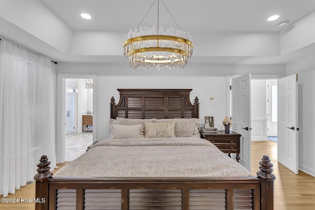 bedroom featuring ensuite bath, light hardwood / wood-style floors, and a chandelier