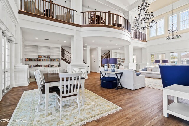 dining space with ornate columns, built in features, a notable chandelier, hardwood / wood-style floors, and a towering ceiling