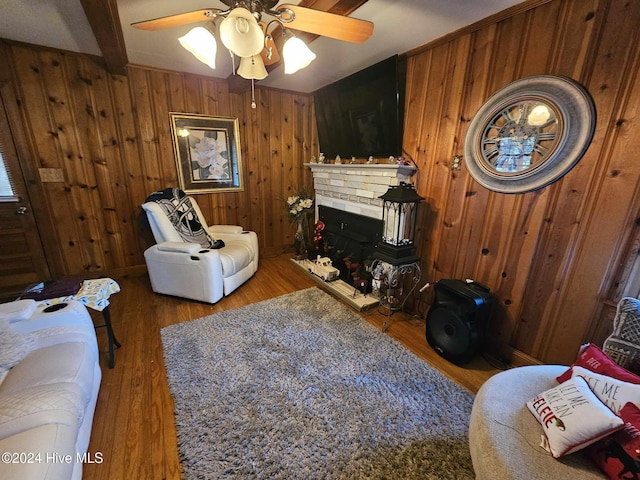 living room with a brick fireplace, hardwood / wood-style flooring, wooden walls, ceiling fan, and beam ceiling